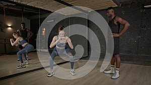 Sporty fit female fitness instructor showing curtsy lunges exercise to man