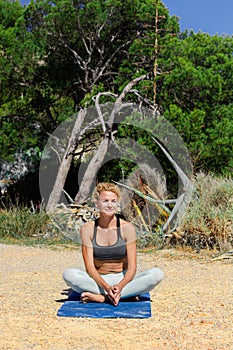 Sporty fit middle aged woman sitting in lotus pose, padmasana, on tropical beach. Female yoga instructor.
