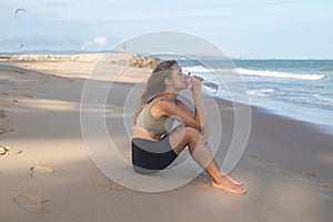 Sporty fit young blonde caucasian woman drinking water on the beach
