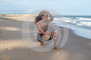 Sporty fit young blonde caucasian woman drinking water on the beach