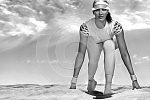 Sporty and fit young woman athlete on startline before running at the desert. Cloudy day on coast. The concept of a