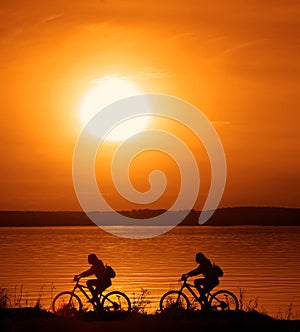 Sporty friends on bicycle on sunset. Silhouette couple cyclist go along coast. Sport in Nature background. Group of people two