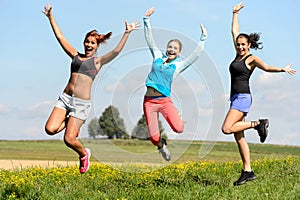 Sporty friends jumping cheerful on sunny meadow