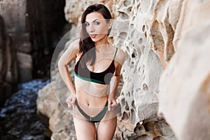 Sporty girl in bikini posing among rocks at sea.