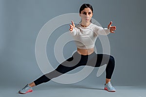 Sporty girl doing bodyweight lateral split squats on grey background