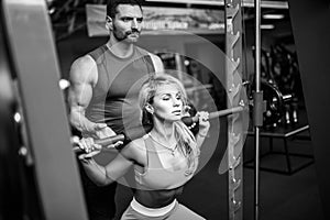 Sporty girl doing squat exercises with assistance of her personal trainer at gym.