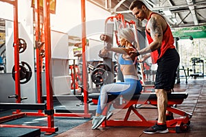 Sporty girl doing weight exercises with assistance of her personal trainer at gym. photo