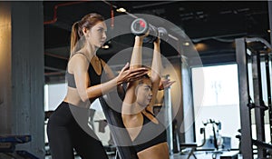 Sporty girl doing weight exercises with the help of her personal trainer at the gym