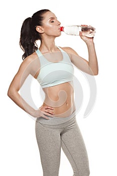 Sporty girl drinking water from a bottle after a workout, fitness training, isolated on white background