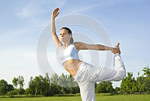 Sporty girl exercising on meadow against the sky