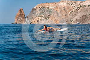 Sporty girl on a glanders surfboard in the sea on a sunny summer day. In a striped swimsuit, lying on his stomach