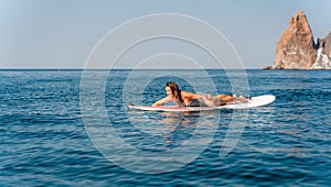 Sporty girl on a glanders surfboard in the sea on a sunny summer day. In a striped swimsuit, lying on his stomach