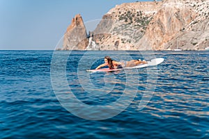 Sporty girl on a glanders surfboard in the sea on a sunny summer day. In a striped swimsuit, lying on his stomach