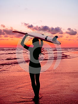 Sporty girl go to surfing. Woman in wetsuit and red sunset or sunrise on ocean