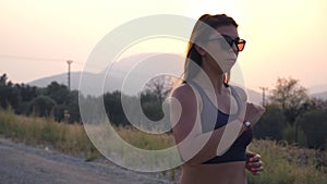 Sporty girl jogging in country road at sunset. Young woman running outdoors. Healthy active lifestyle. Slow motion Close