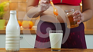 Sporty girl puts honey in a glass of almond milk, slow motion