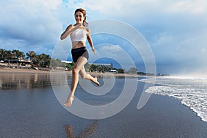 Sporty girl running by beach along sea surf