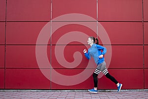 Sporty girl runs against a red wall in the street, a woman jogging in sportswear outdoors, copy space