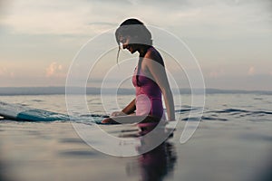 sporty girl sitting on surfboard in water in ocean