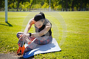 Sporty girl stratching muscles on yoga mat on stadium green lawn. Sport, physical training, healthy way of life, fitness concept.