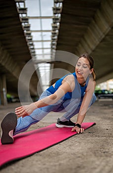 Sporty girl stretching muscles crouching on pink mat in parking lot