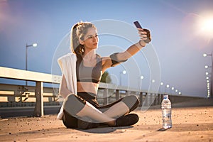 Sporty girl taking a self portrait photography while sitting on sidewalk at night.