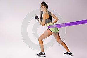 Sporty girl in top and sharts doing exercises with a harness of resistance on a white background with empty side space.