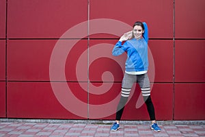 Sporty girl is training against a red wall in the street, a woman is doing warm-up in sportswear outdoors, copy space