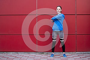 Sporty girl is training against a red wall in the street, a woman is doing warm-up in sportswear outdoors, copy space