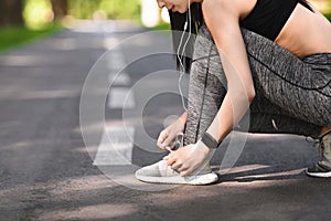 Sporty girl tying shoes laces before running, getting ready for jogging outdoors