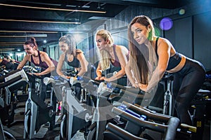 Sporty girls riding exercise bikes in gym.