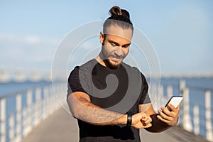 sporty guy checking pulse on fitness tracker holding smartphone outdoor