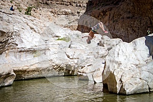 Sporty guy doing backflip off cliff into lake in an oasis in middle of Oman desert