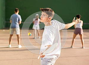 Sporty guy playing pelota with wooden racket on open fronton court