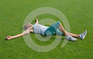Sporty guy relaxing on green training field