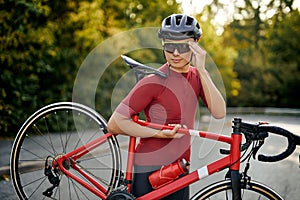 Sporty guy in sportive clothes, protective helmet and glasses carrying bike, posing