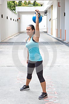 Sporty hispanic woman in blue lifting blue kettlebell for routine outdoors