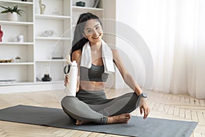 Sporty lady sitting on sports mat with bottle of water