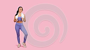 Sporty lady in wireless headphones with towel around neck standing on pink studio background, panorama with copy space
