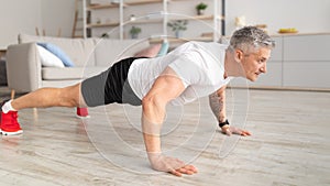 Sporty lifestyle for senior people concept. Mature man planking, exercising in living room interior