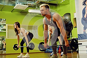Sporty male and two females doing squats with barbells in a gym.