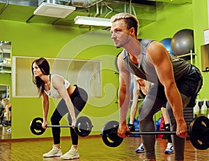 Sporty male and two females doing squats with barbells in a gym.