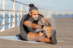 Sporty man in activewear practices seated forward bend by sea