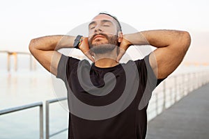 Sporty man in black t-shirt closes eyes touching neck outdoor