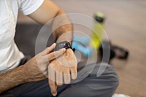 Sporty man checking pulse on smartwatch after workout inside