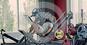 Sporty man doing exercises with leg press machine at fitness gym, hard squats workout