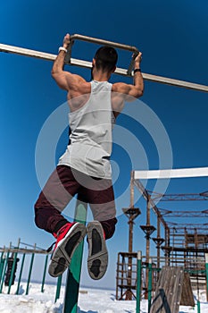 Sporty man doing pull up exercise outdoors