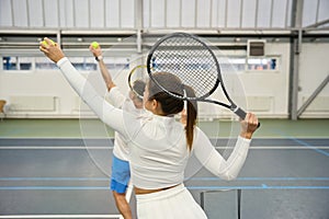 Sporty man instructor teaching woman to serve tennis ball focusing on technique