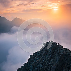 Sporty man on the mountain peak looking on mountain valley with sunbeams at colorful sunset in autumn in Europe. Landscape with