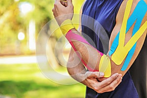 Sporty man with physio tape applied on arm outdoors, closeup